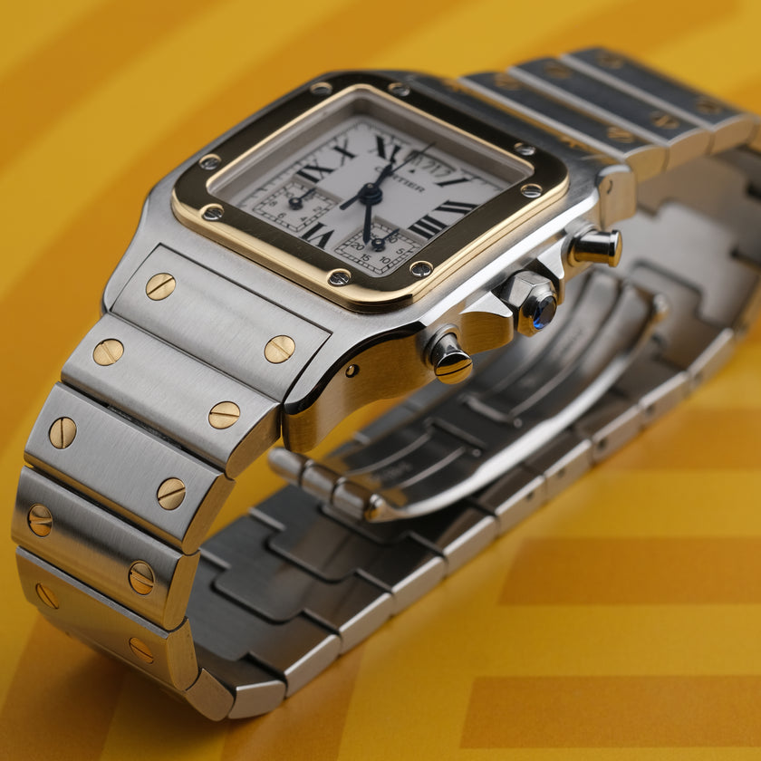A Cartier watch with a silver-toned stainless steel case and bracelet, a gold-toned bezel, and a white dial with Roman numerals, set against a yellow background.