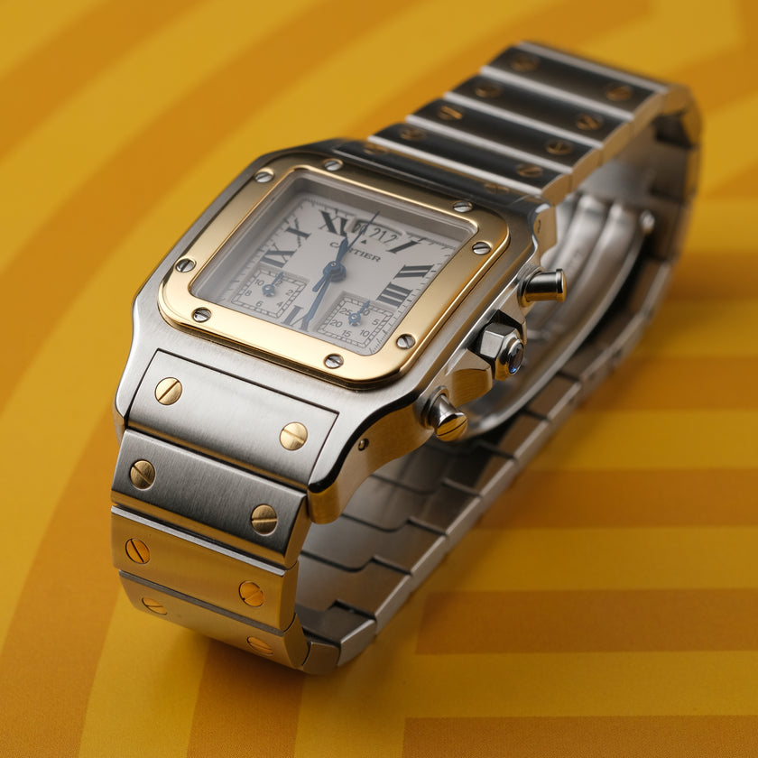 A Cartier watch with a silver-toned stainless steel case and bracelet, a gold-toned bezel, and a white dial with Roman numerals, set against a yellow background.