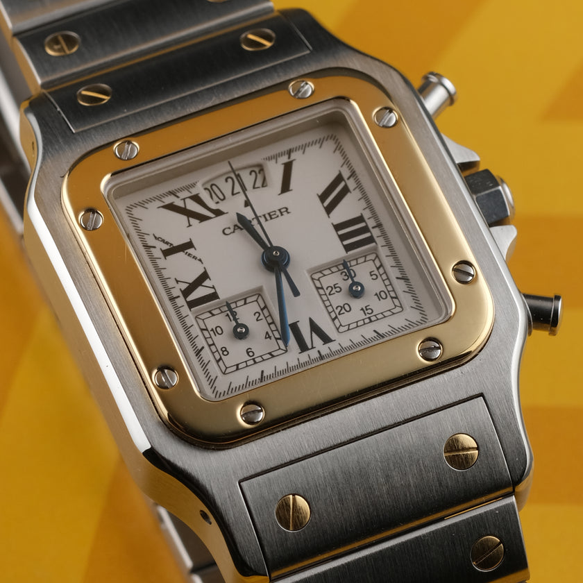A Cartier watch with a silver-toned stainless steel case and bracelet, a gold-toned bezel, and a white dial with Roman numerals, set against a yellow background.