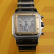 A Cartier watch with a silver-toned stainless steel case and bracelet, a gold-toned bezel, and a white dial with Roman numerals, set against a yellow background.