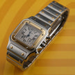 A Cartier watch with a silver-toned stainless steel case and bracelet, a gold-toned bezel, and a white dial with Roman numerals, set against a yellow background.