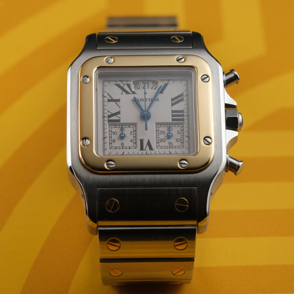 A Cartier watch with a silver-toned stainless steel case and bracelet, a gold-toned bezel, and a white dial with Roman numerals, set against a yellow background.