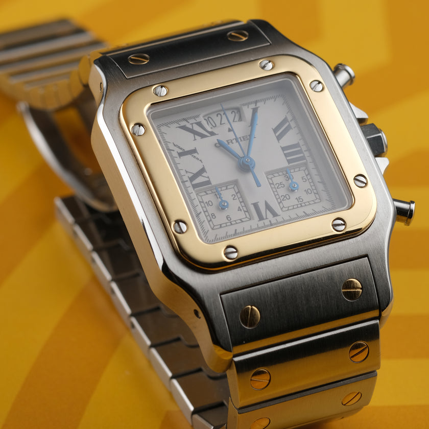 A Cartier watch with a silver-toned stainless steel case and bracelet, a gold-toned bezel, and a white dial with Roman numerals, set against a yellow background.
