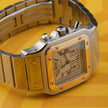 A Cartier watch with a silver-toned stainless steel case and bracelet, a gold-toned bezel, and a white dial with Roman numerals, set against a yellow background.