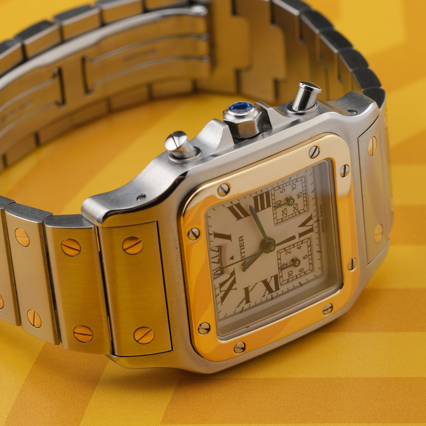 A Cartier watch with a silver-toned stainless steel case and bracelet, a gold-toned bezel, and a white dial with Roman numerals, set against a yellow background.