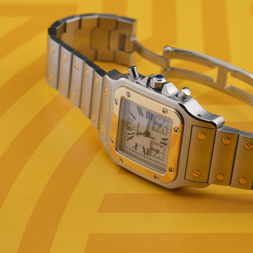 A Cartier watch with a silver-toned stainless steel case and bracelet, a gold-toned bezel, and a white dial with Roman numerals, set against a yellow background.