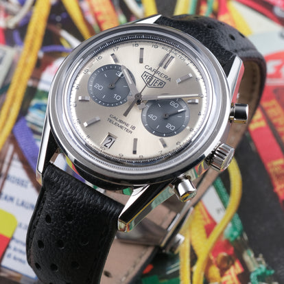 A TAG Heuer Carrera 18 Telemeter wristwatch with a silver-toned stainless steel case, a champagne dial, black subdials, and a black leather strap, shown in a close-up shot.