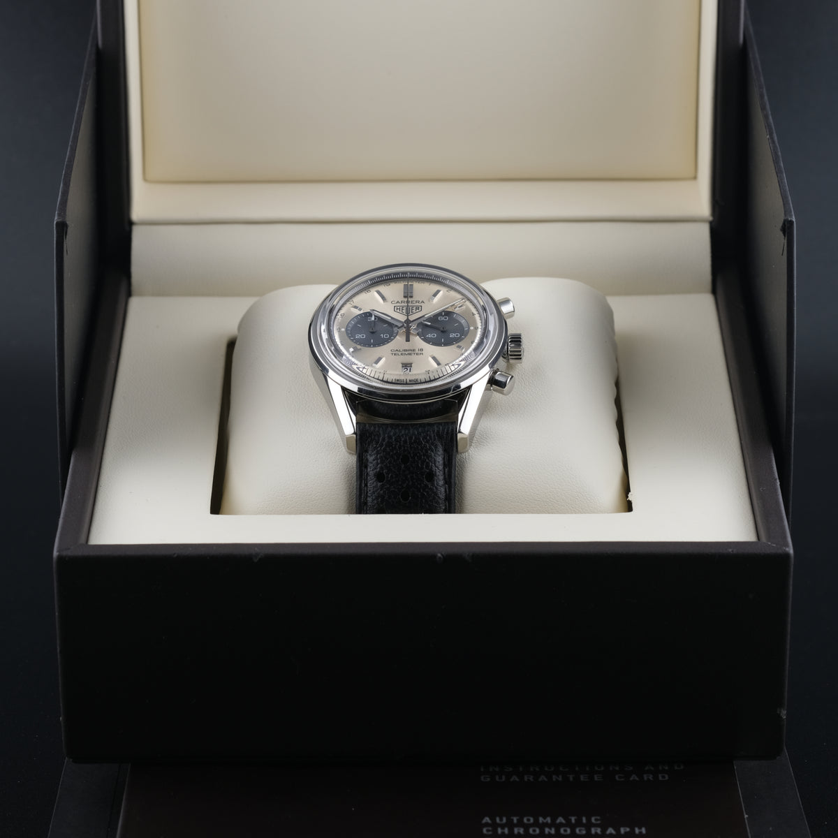 A TAG Heuer Carrera 18 Telemeter wristwatch with a silver-toned stainless steel case, a champagne dial, black subdials, and a black leather strap, shown in a close-up shot.