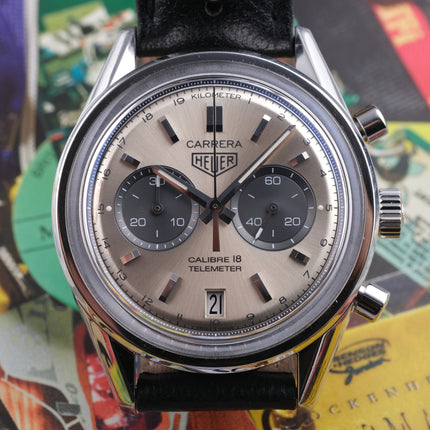 A TAG Heuer Carrera 18 Telemeter wristwatch with a silver-toned stainless steel case, a champagne dial, black subdials, and a black leather strap, shown in a close-up shot.