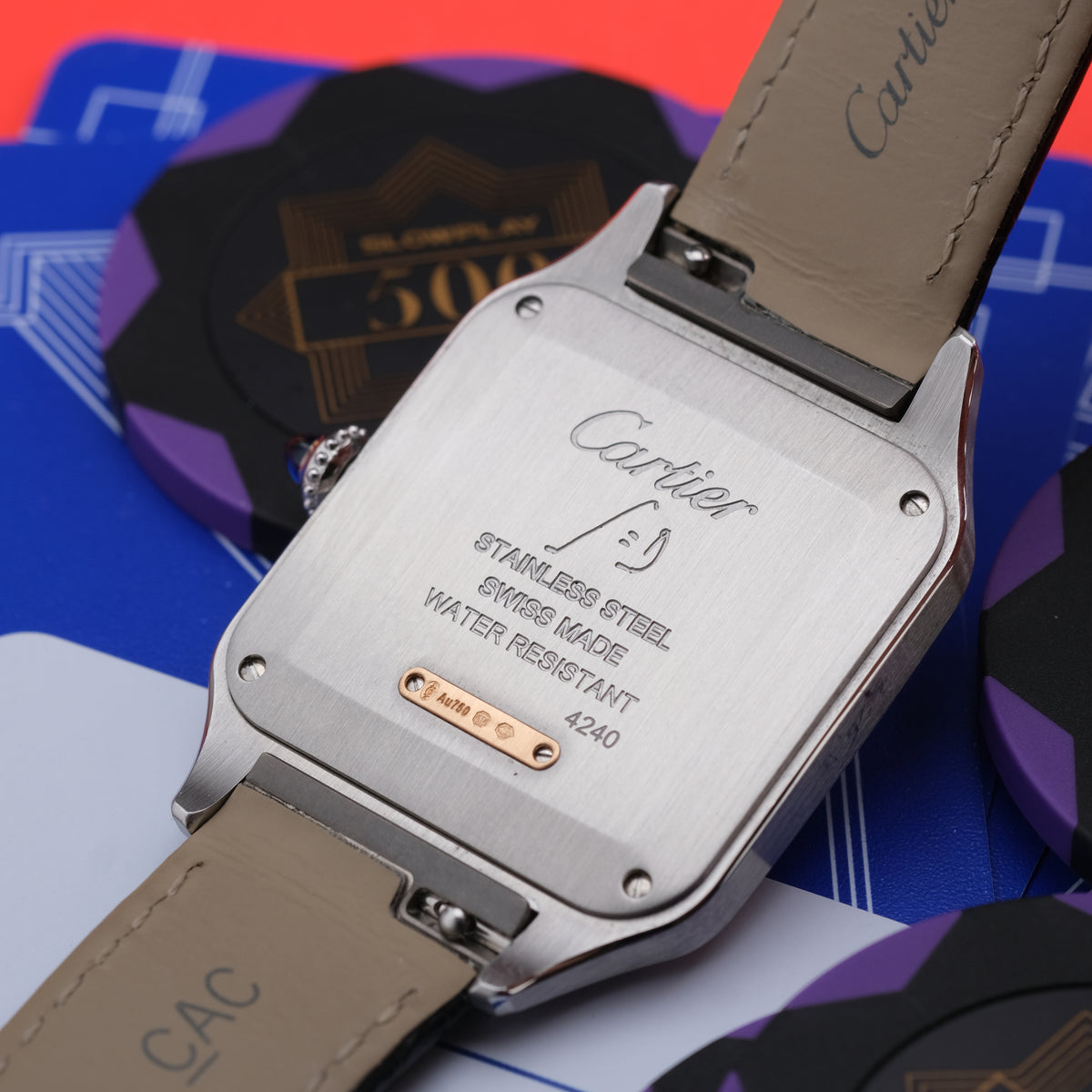 Close-up of the back of a Cartier watch with a stainless steel case and beige leather strap, resting on colorful branded cards.