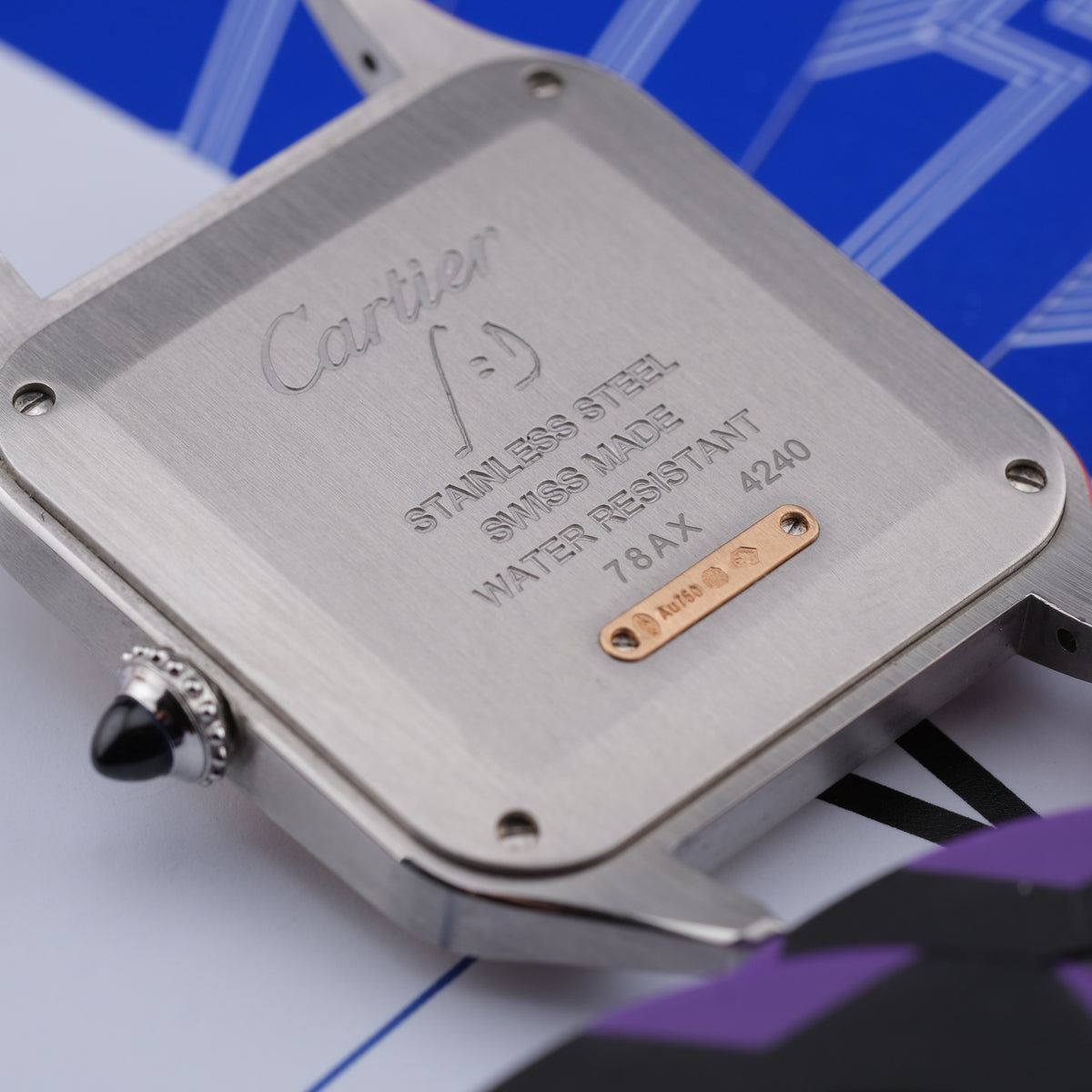 Close-up of the brushed stainless steel back of a Cartier watch, showing engraved text including 'Cartier', 'STAINLESS STEEL', 'SWISS MADE', and a small gold-tone plate with 'CARTIER' and a logo.