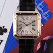 A Cartier Santos watch with a square stainless steel case, gold-tone bezel accents, a white dial with black Roman numerals, and a black alligator leather strap. The watch is centered against a colorful background featuring playing card suits.