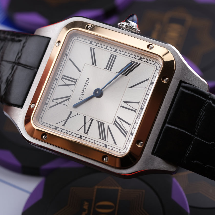 A Cartier Santos watch with a square stainless steel case, rose gold-toned bezel, white dial with black Roman numerals, and a black leather strap, shown in a close-up product shot.