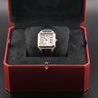 A Cartier Santos watch with a silver-toned square case, gold-tone bezel accents, and a black leather strap, displayed inside an open red Cartier presentation box with black velvet cushioning.