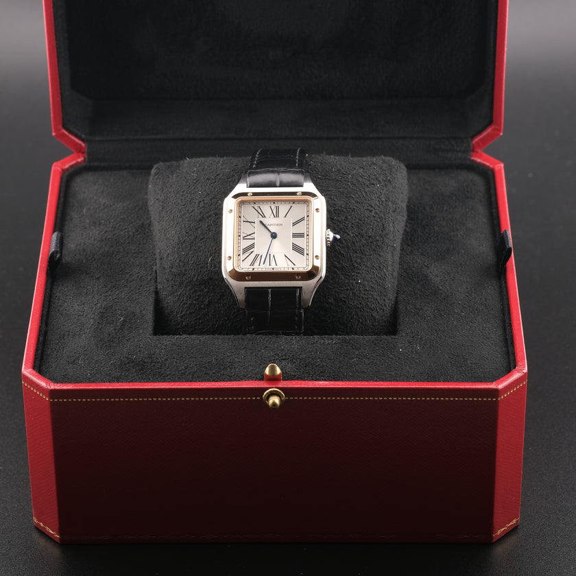 A Cartier Santos watch with a silver-toned square case, gold-tone bezel accents, and a black leather strap, displayed inside an open red Cartier presentation box with black velvet cushioning.