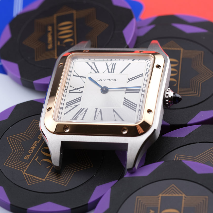 A Cartier Santos watch with a silver-toned stainless steel case, gold-tone accents, and a white dial with Roman numerals, resting on a stack of black and purple poker chips.