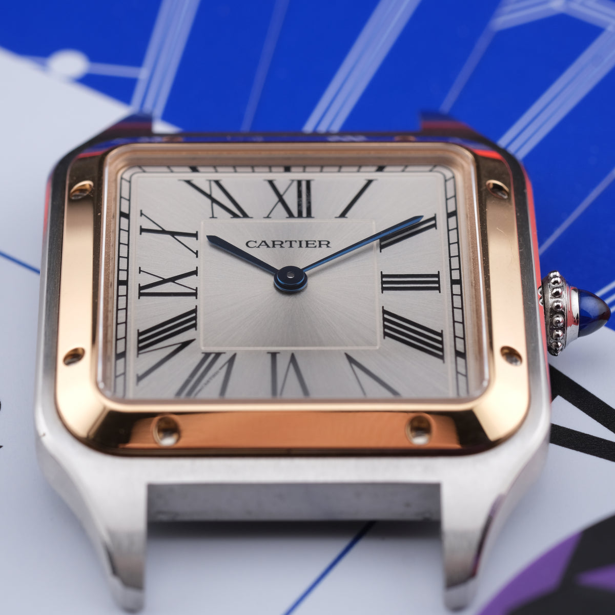 A close-up shot of a Cartier Santos watch with a silver-toned stainless steel case, rose gold bezel, and a white dial with black Roman numerals.
