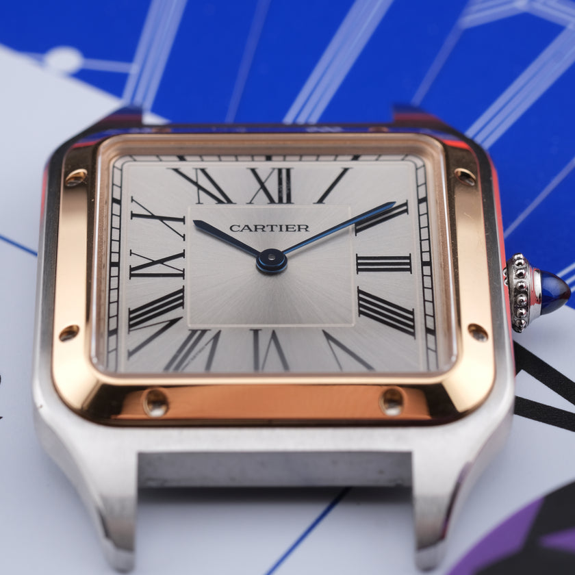 A close-up shot of a Cartier Santos watch with a silver-toned stainless steel case, rose gold bezel, and a white dial with black Roman numerals.