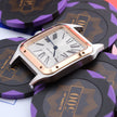 A rectangular analog watch with a silver-toned case, rose gold-toned bezel, and white dial with Roman numerals, styled on top of black and purple poker chips.