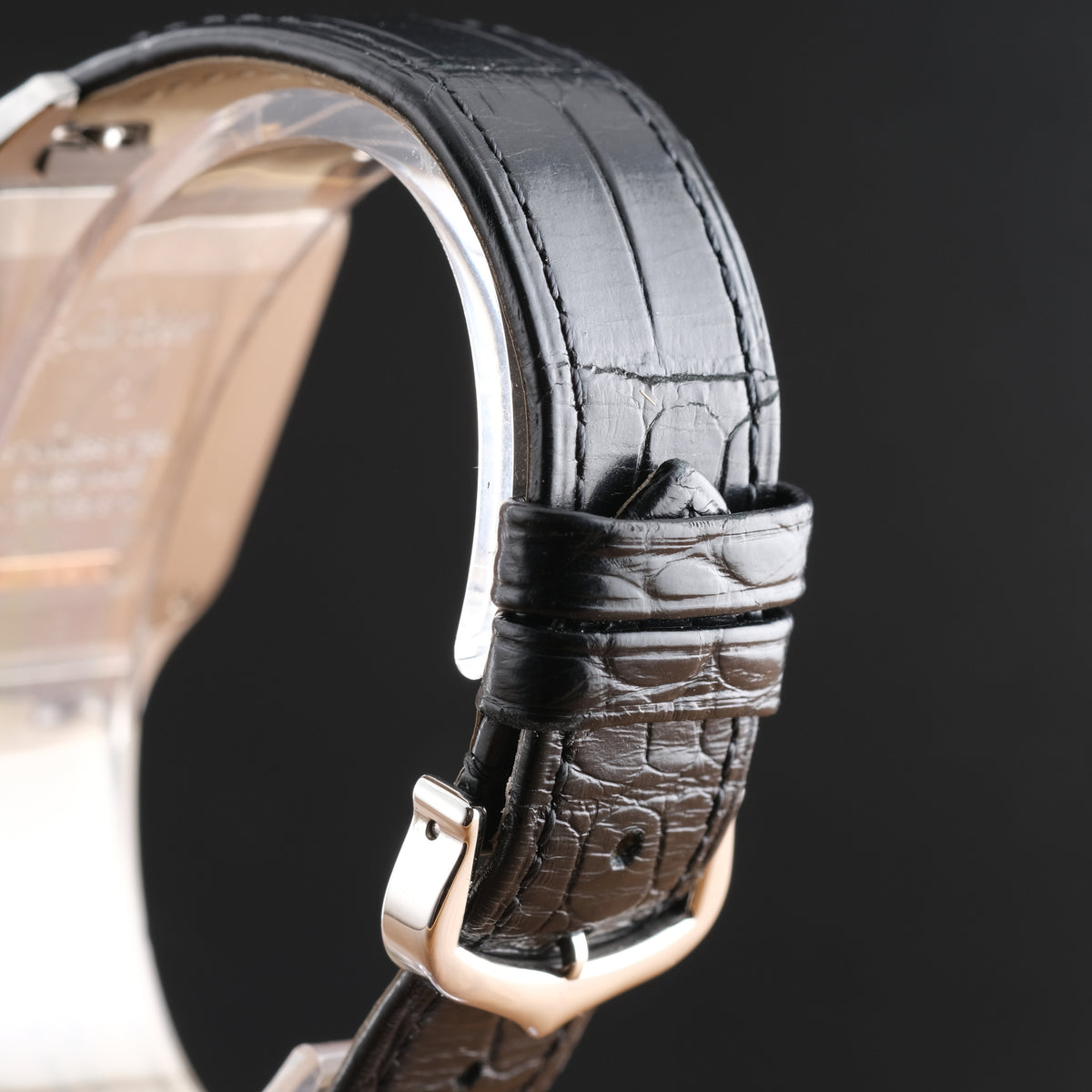 Close-up of a black alligator leather watch strap with a textured crocodile pattern, secured with a polished rose gold buckle on a watch case.
