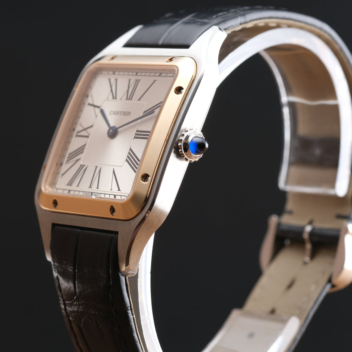 Cartier Santos watch with a silver-toned stainless steel case, gold-toned bezel, white dial with Roman numerals, and a black leather strap, shown on a black background.