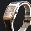 Cartier Santos watch with a silver-toned stainless steel case, gold-toned bezel, white dial with Roman numerals, and a black leather strap, shown on a black background.