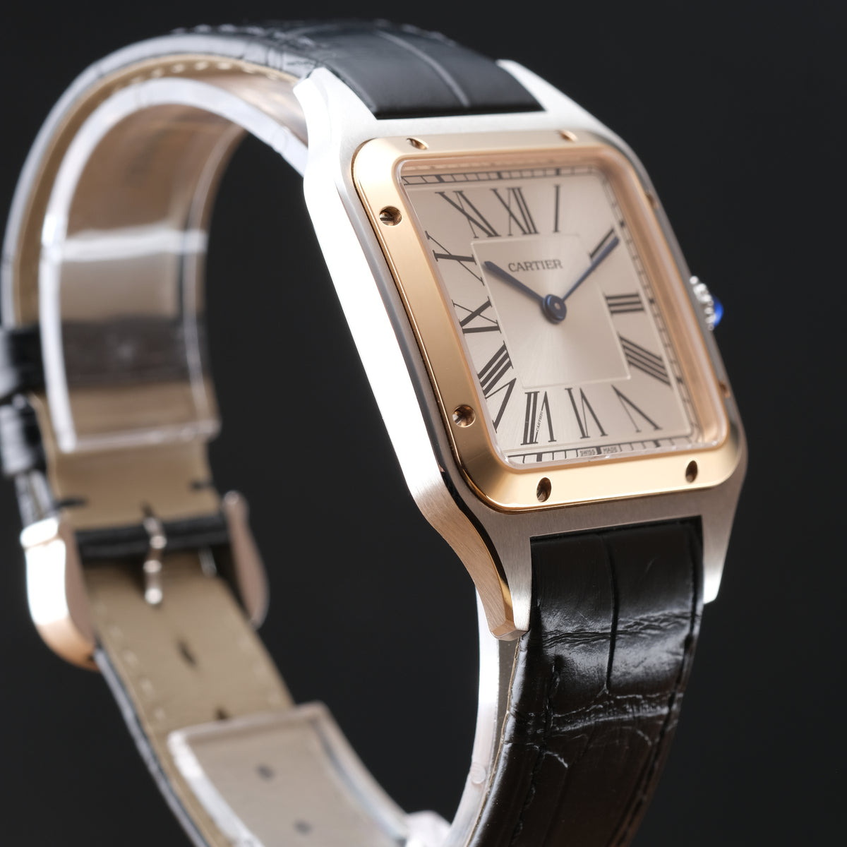 Cartier Santos watch with a silver-toned stainless steel case, gold-toned bezel, cream dial with Roman numerals, and a black leather strap, shown on a dark background.