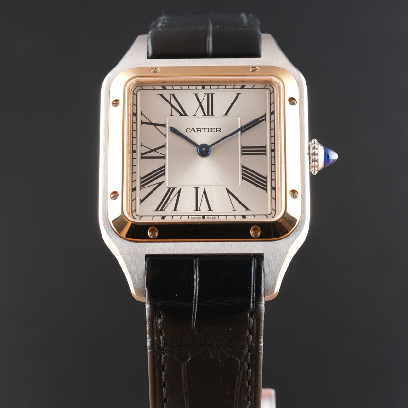 A Cartier Santos watch with a square stainless steel case, rose gold-toned bezel, white dial with black Roman numerals, and a black leather strap, shown against a dark gray background.