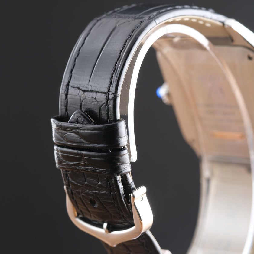 Close-up of a black crocodile-embossed leather watch strap attached to a silver-toned metal watch case, shown against a dark background.