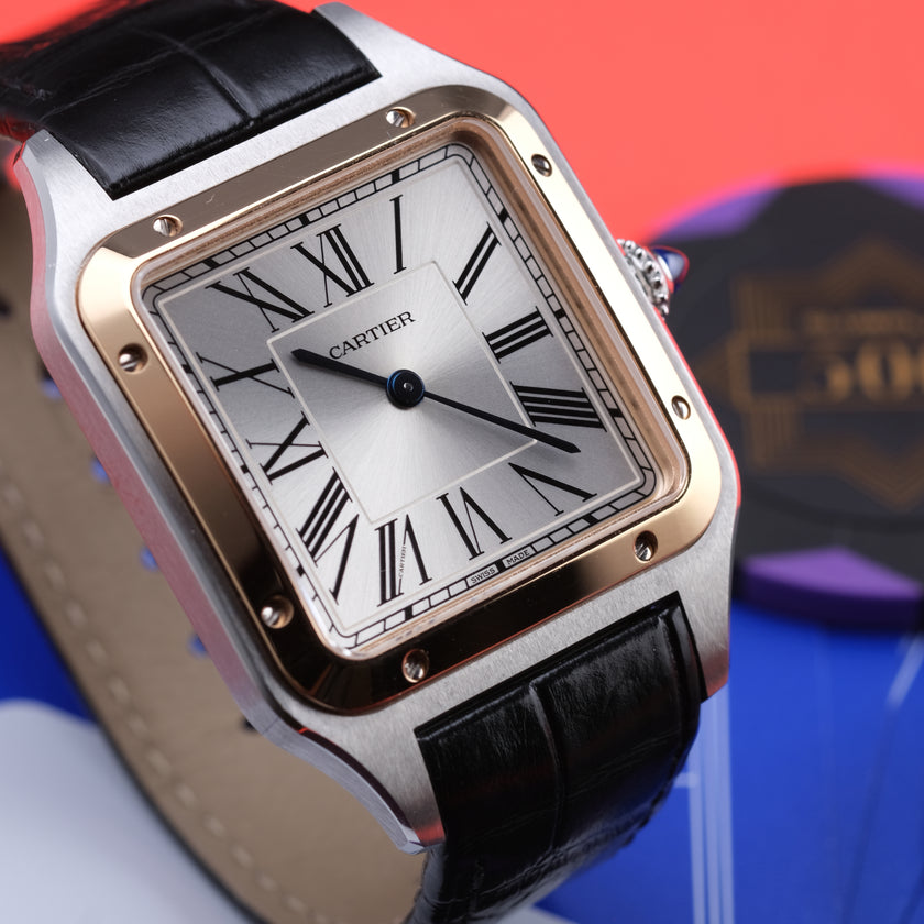 A Cartier watch with a square silver-toned case, black leather strap, and a silver dial with black Roman numerals, shown close-up against a colorful blurred background.